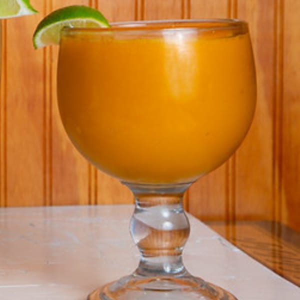 A large glass of orange-colored Mexican drink, possibly a mango margarita, garnished with a lime wedge.