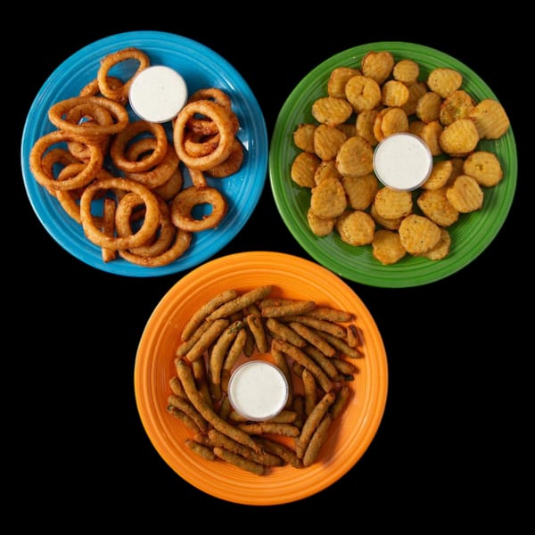 Three colorful plates of fried appetizers: onion rings, fried pickles, and fried green beans, each with ranch.