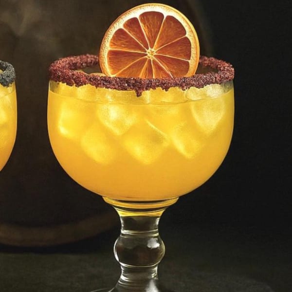 A vibrant orange Mexican cocktail with a chili-lime rim and an orange slice garnish.