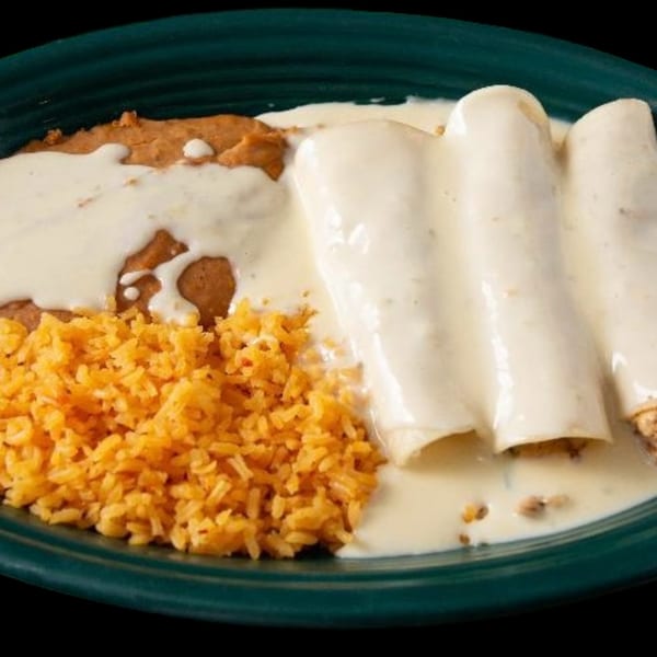 Three enchiladas covered in white sauce, served with refried beans and orange rice on a green plate.