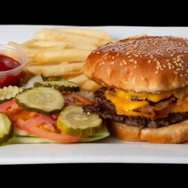 Cheeseburger with bacon, fries, ketchup, and a side salad with pickles, tomatoes, and lettuce.