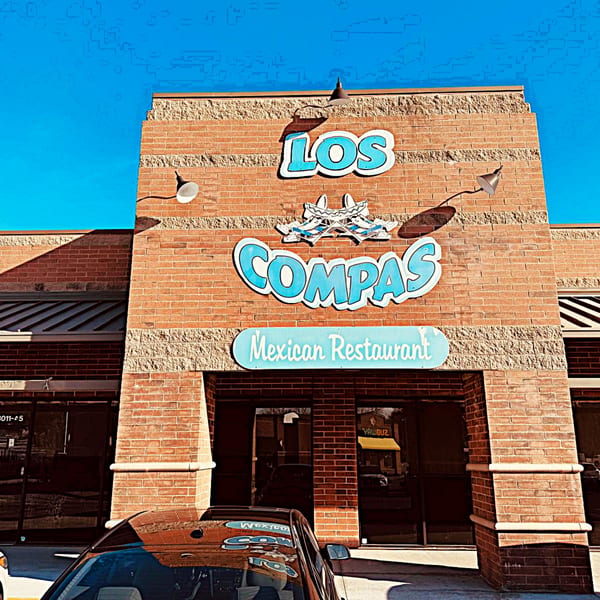 Exterior of Los Compas Mexican Restaurant with brick facade and blue signage under a clear sky.
