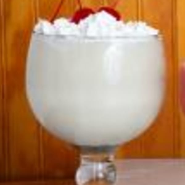 A white drink with whipped cream and two red cherries in a large stemmed glass.