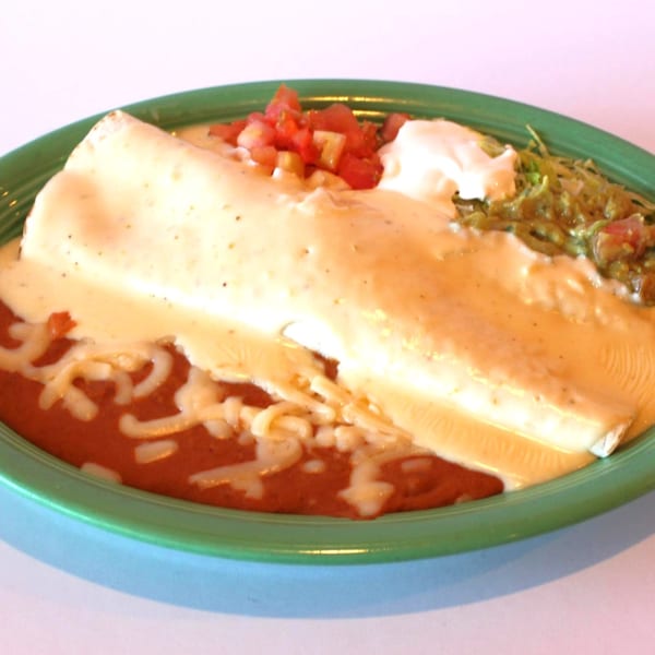 A large burrito covered in white cheese sauce, with refried beans, guacamole, and pico de gallo.