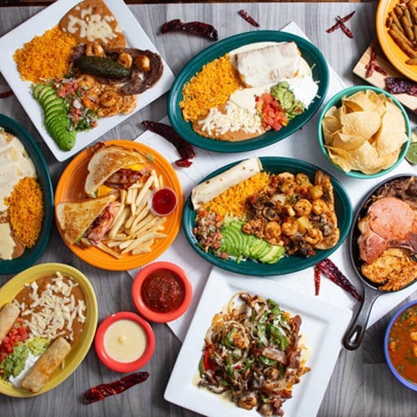 A vibrant spread of various Mexican dishes, including burritos, fajitas, and taquitos, on a wooden table.