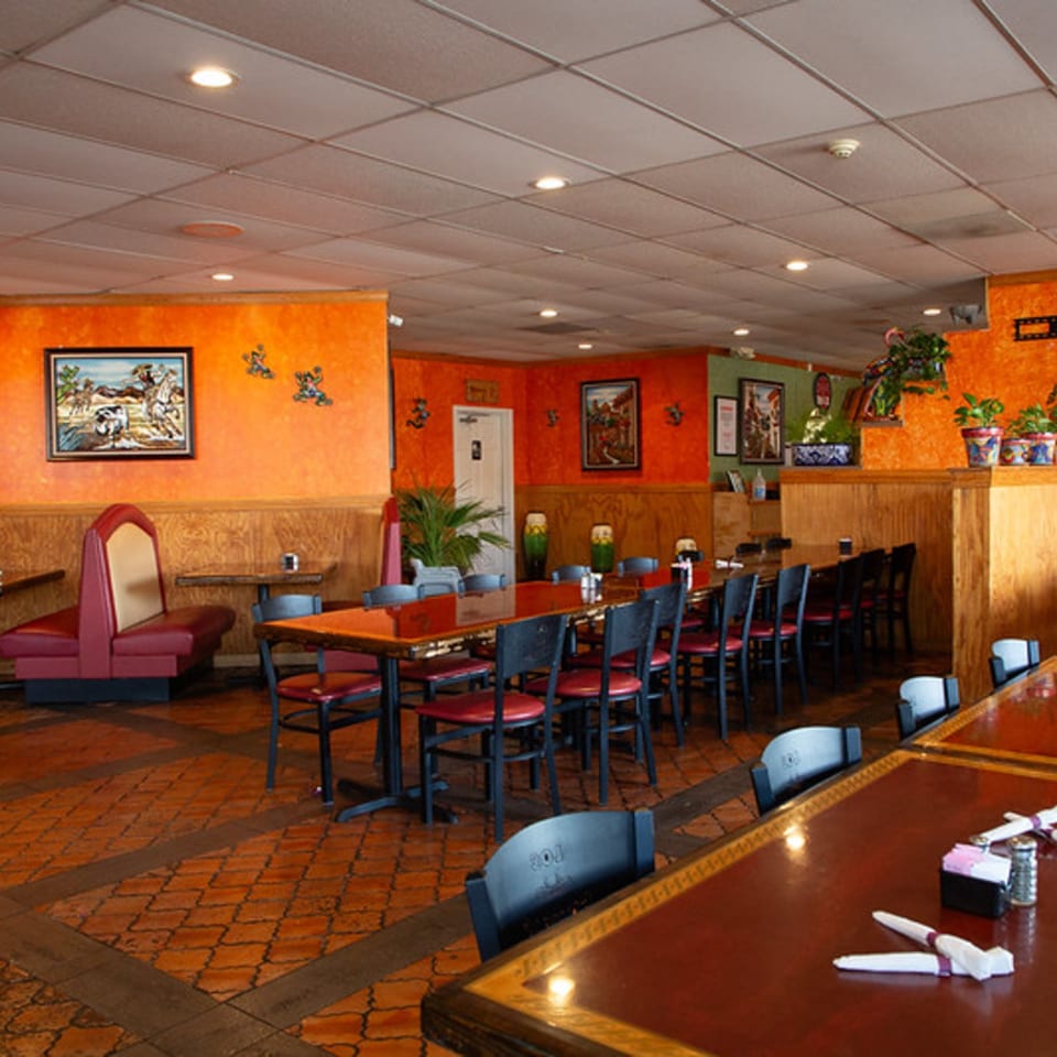 The vibrant dining room of Los Compas Independence, featuring orange walls, booths, and long tables.