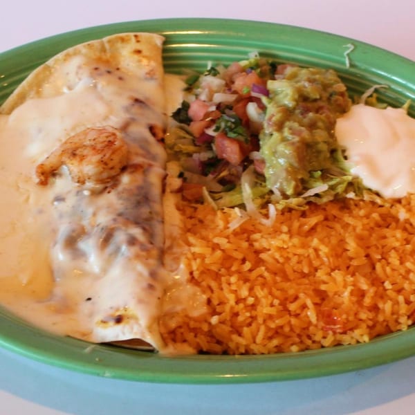 Shrimp enchilada with white sauce, rice, guacamole, pico de gallo, and sour cream on a green plate.