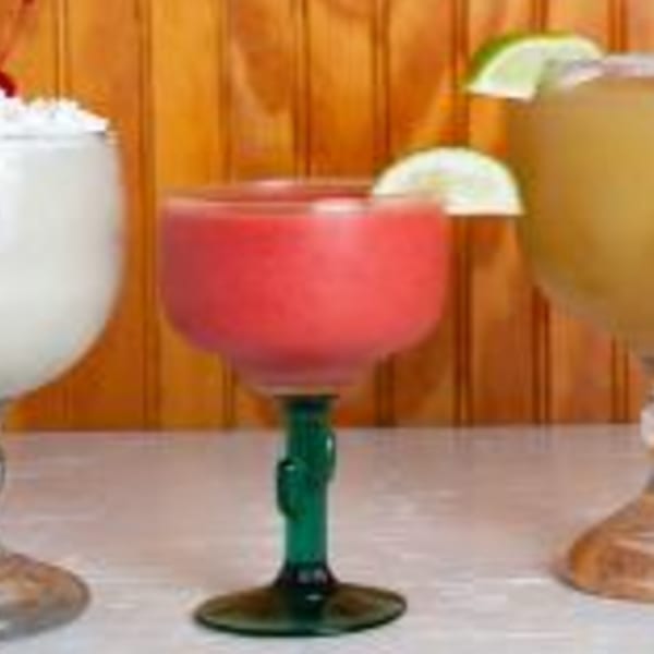 Three margaritas in decorative glasses, one white, one red with a lime, and one yellow with a lime.