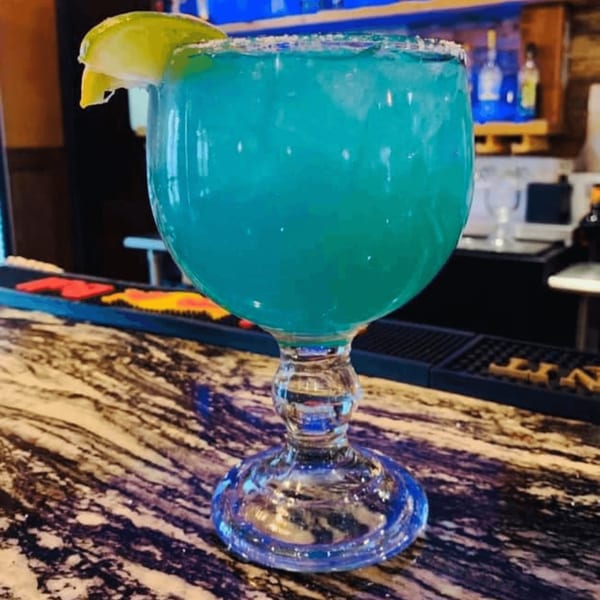 A large blue margarita with a lime wedge and salted rim sits on a marble bar.