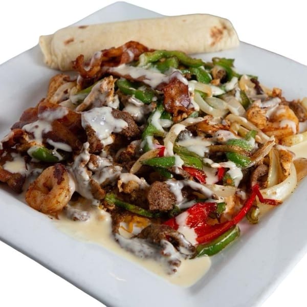 Los Compas Independence's fajita-style dish with meat, shrimp, peppers, onions, and white sauce, with a tortilla.