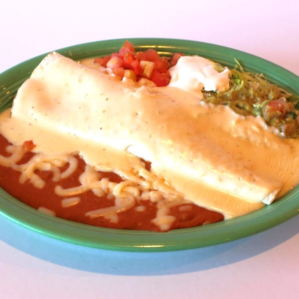 Los Compas' Mexican burrito covered in white cheese sauce, with red sauce, guacamole, and sour cream.