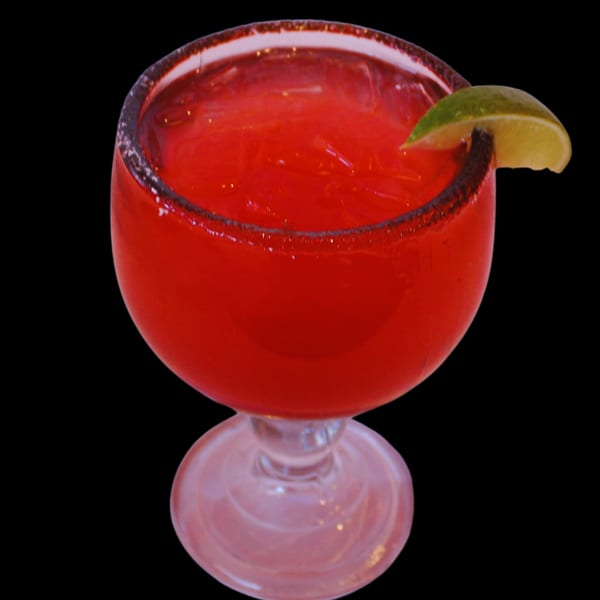 Red margarita with a salted rim and lime wedge, served in a large goblet.