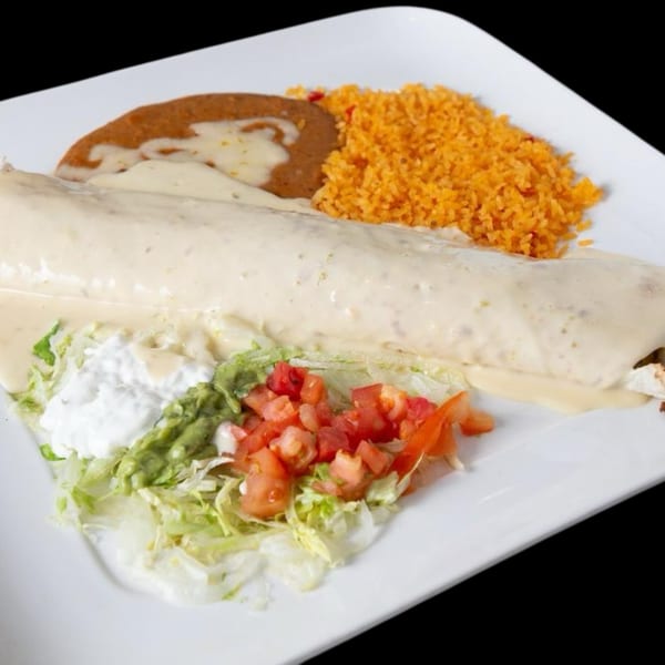 A large burrito covered in white cheese sauce, with rice, refried beans, lettuce, guacamole, and diced tomatoes.